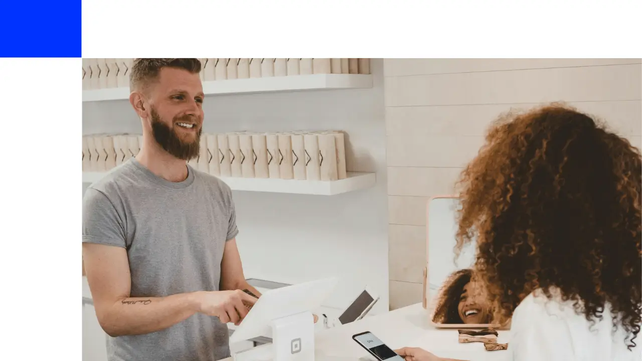 Homem e mulher mexendo em dispositivos que estão em um display em alguma loja. Ele é branco e ela negra.