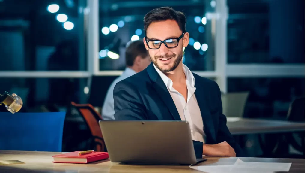 Homem com o computador aberto sorrindo após ver uma boa base de conhecimento